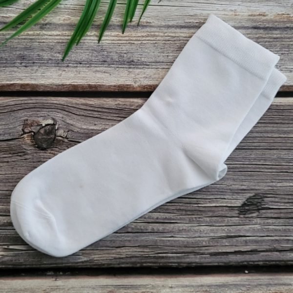 one pair of white socks on wood table with green leaves